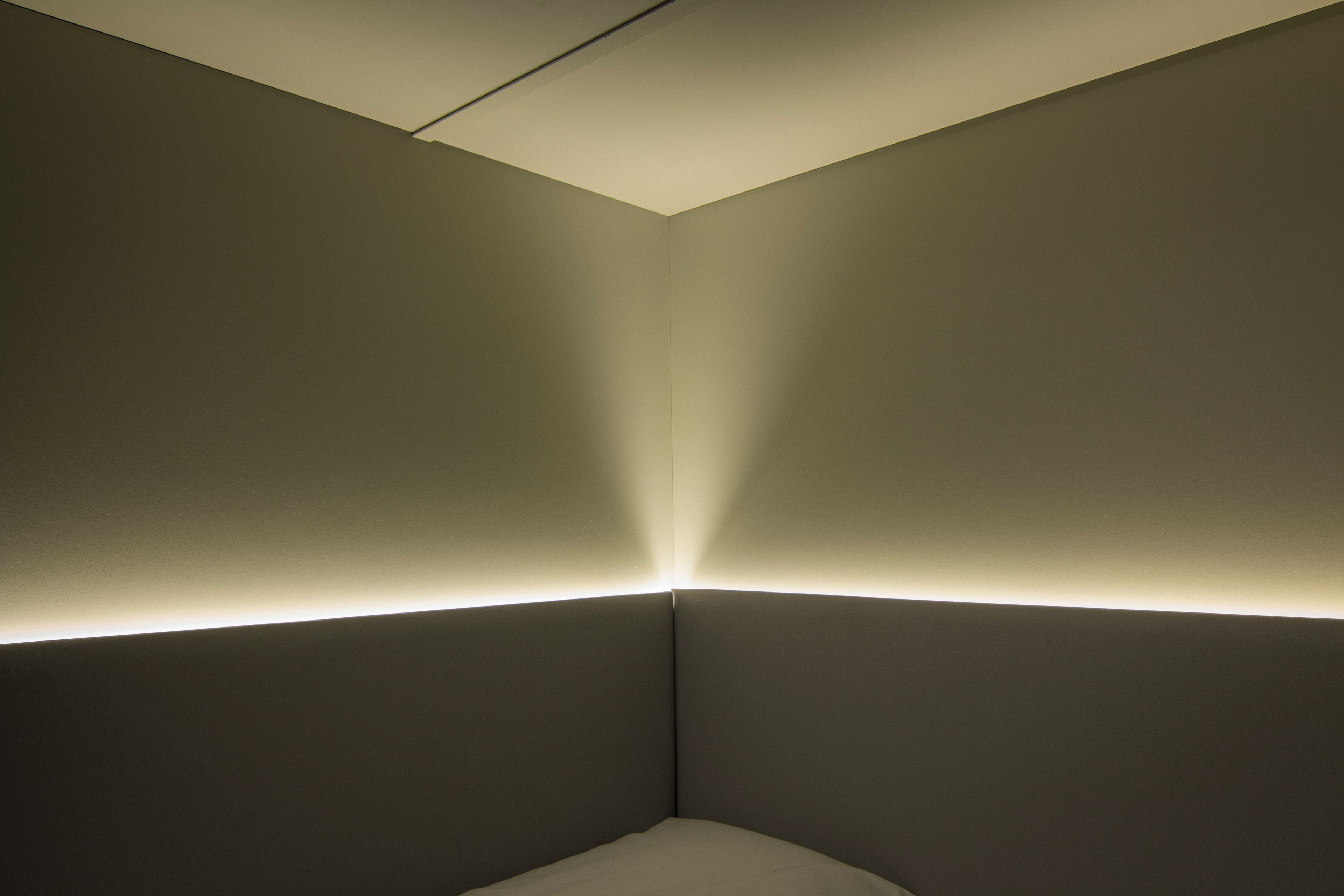 Una esquina de una habitación con techo inclinado y una tira de luz a lo largo del borde inferior.