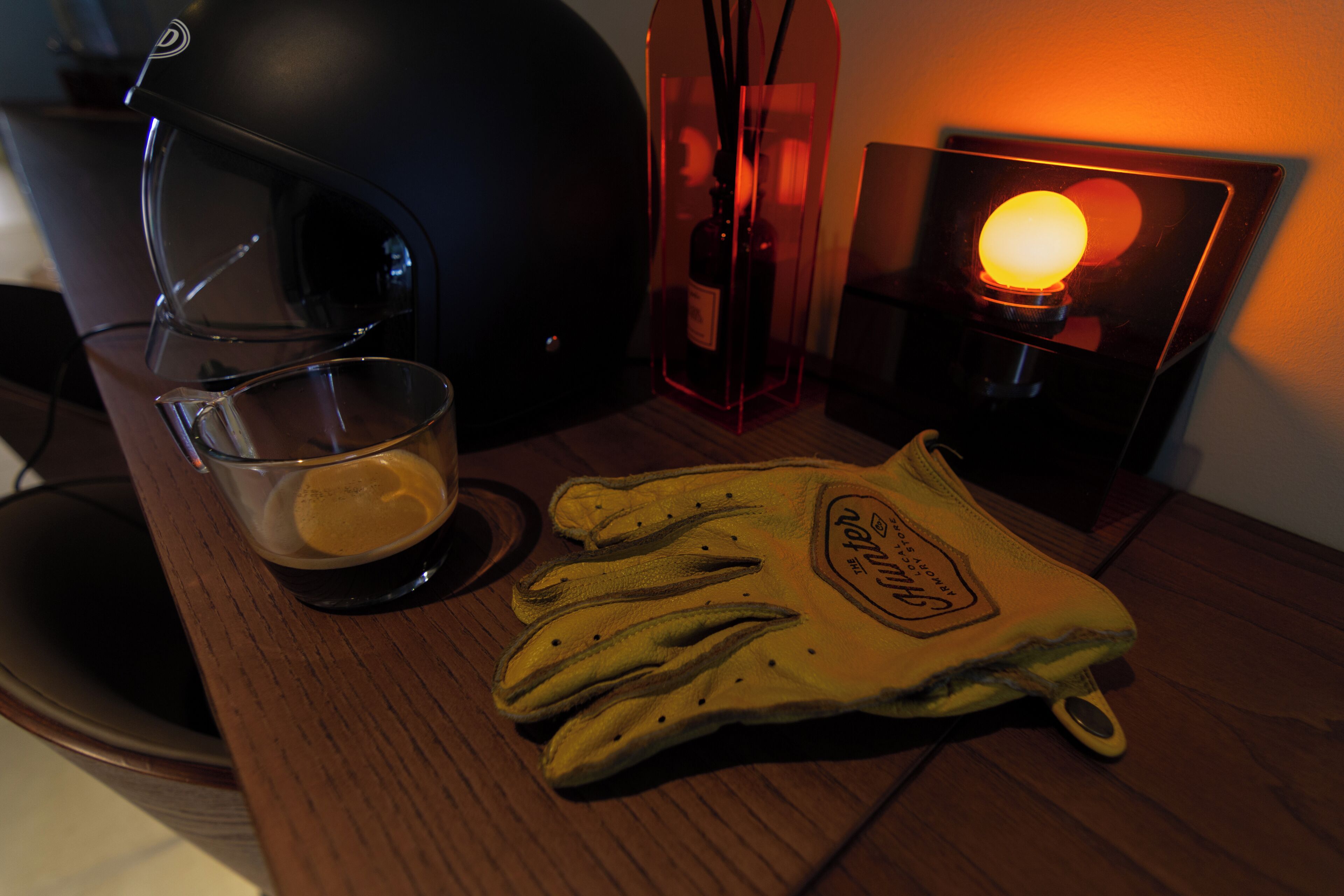 Un comptoir de cuisine avec une machine à café, une tasse de café, une paire de gants et une bougie allumée.