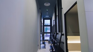 A narrow hallway with a ceiling light fixture, a door at the end, and a bed in a room to the right. - Hostel Superlativo Vialia I (Málaga)