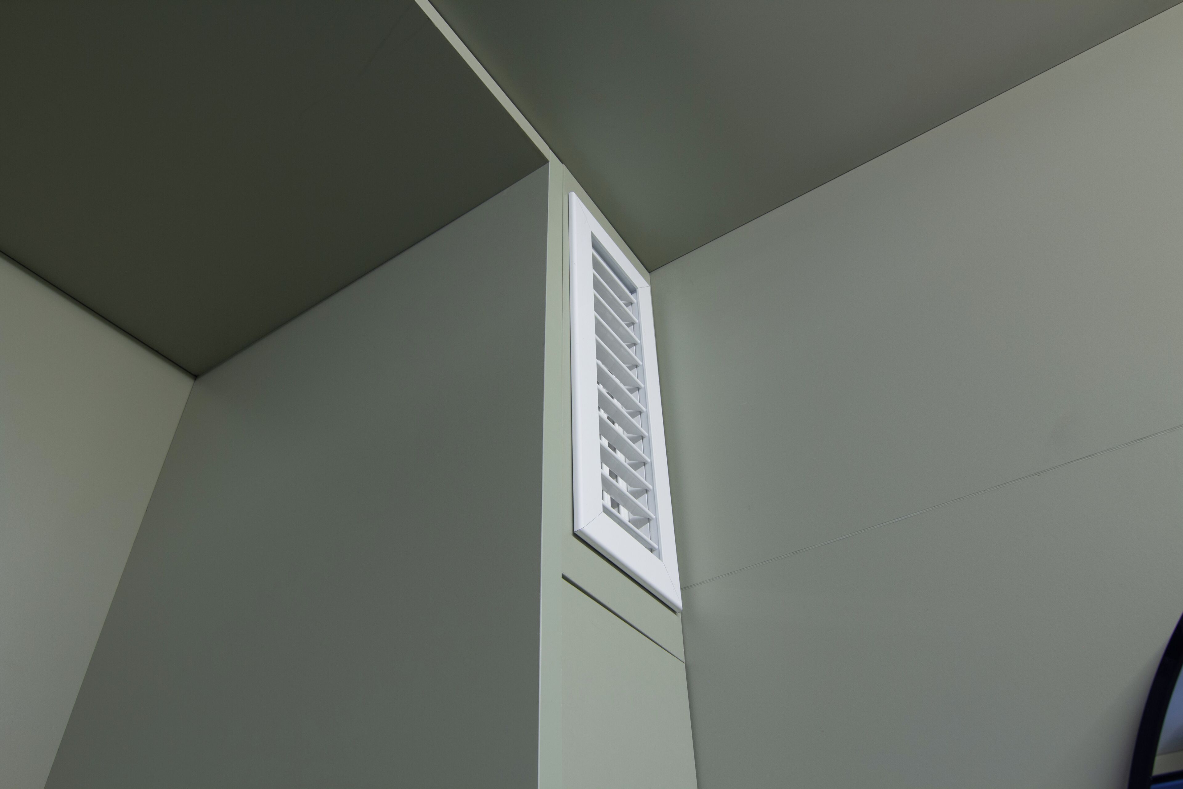 A corner of a room with a white vent on the wall.
