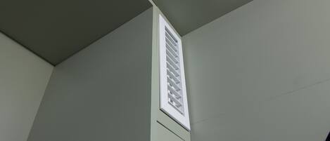A corner of a room with a white vent on the wall.