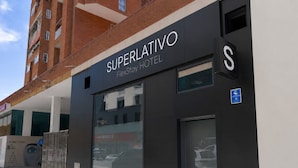Un hotel llamado 'Superlativo FlexStay Hotel' con una fachada moderna, amplias ventanas y un estacionamiento visible.