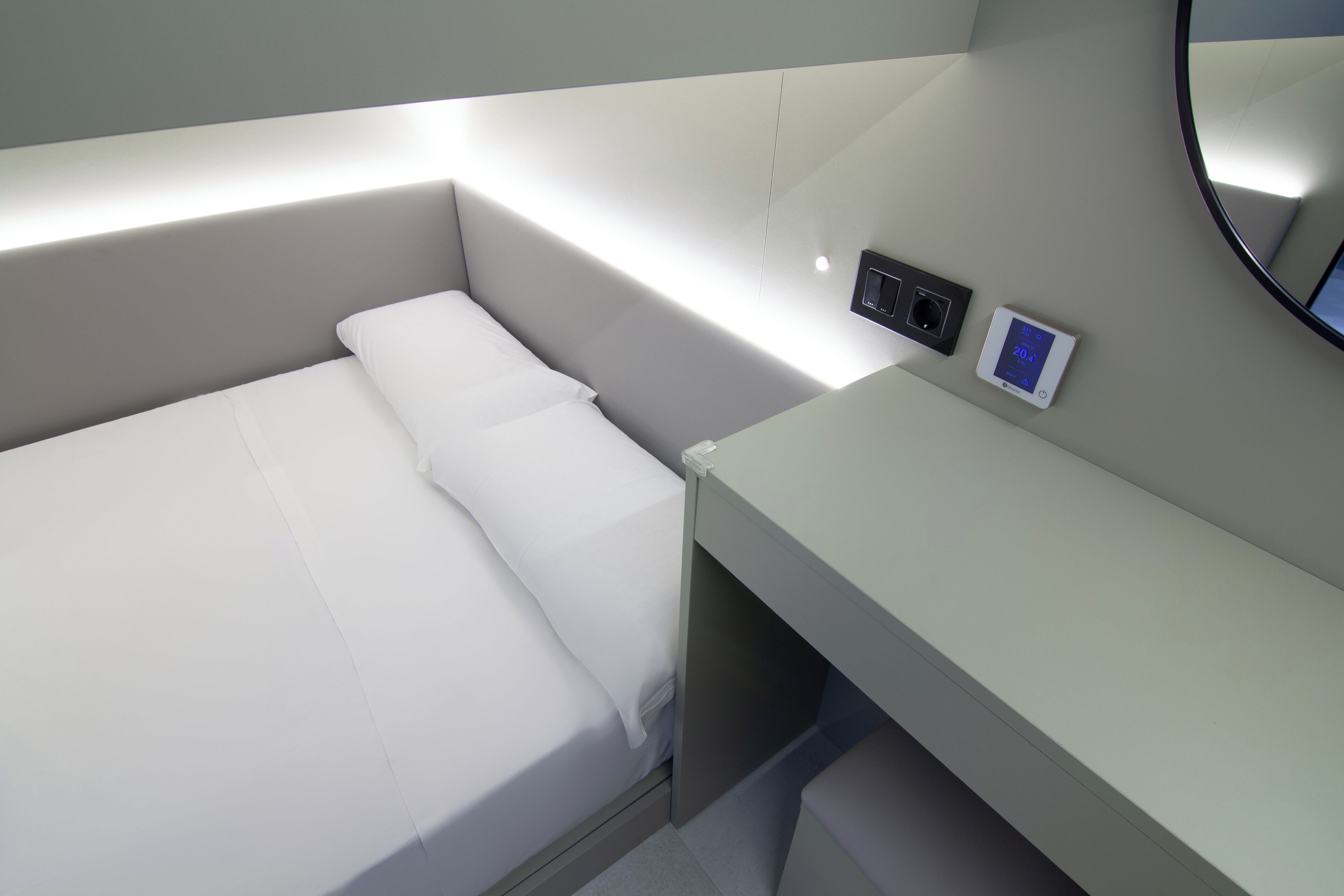 Une chambre d’hôtel moderne équipée d’un lit, d’un panneau de commande près du lit et d’un miroir fixé au mur.