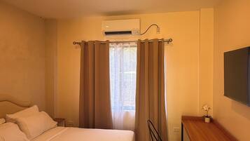 A hotel room with a bed, a desk, a chair, an air conditioning unit, and a window with curtains.
