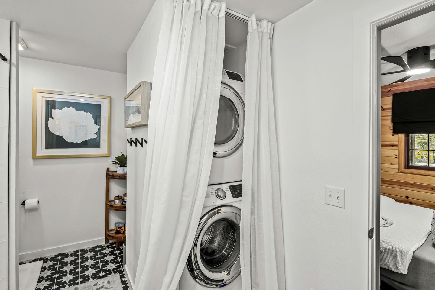A laundry room with two washing machines, a shower curtain, a framed picture, and a small shelf with items.