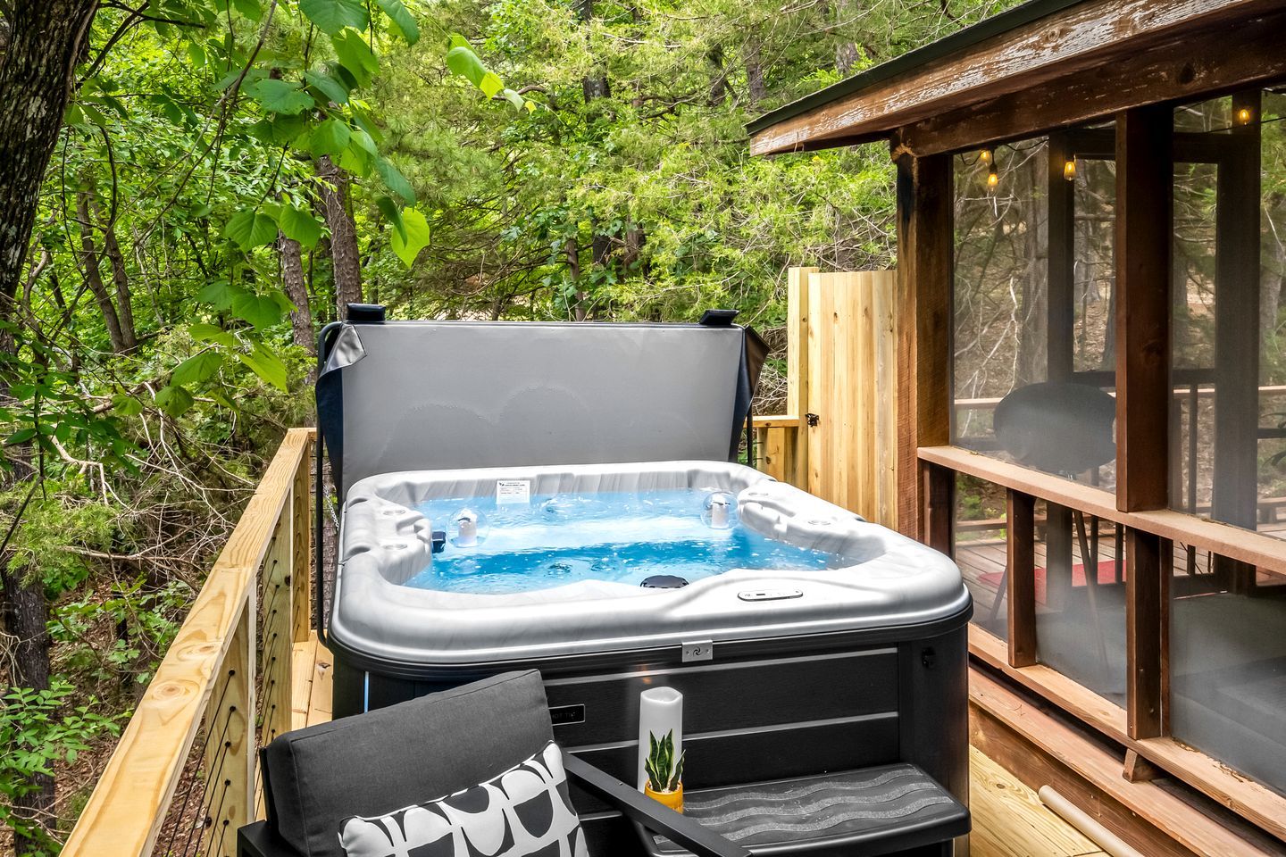 A hot tub on an outdoor deck with a wooden railing, surrounded by greenery.