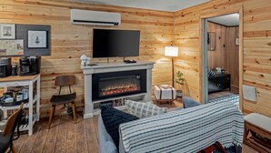 Una habitación acogedora con chimenea, un televisor de pantalla plana, un escritorio con cafeteras y una zona de estar cómoda.