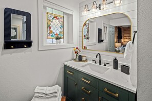 A bathroom with a white sink, dark green cabinets, a large mirror, and a stained glass window. - Romantic and Secluded Log Cabin with Private Hot Tub in Eureka Springs, Arkansas (Eureka Springs)