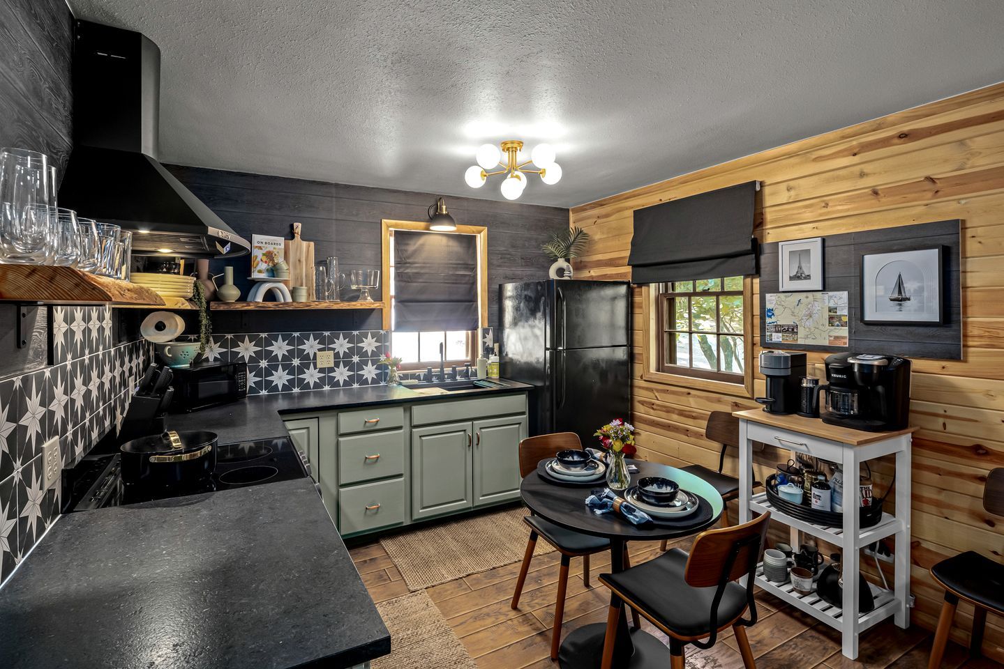 Una cocina compacta con un refrigerador negro, una mesa de comedor con sillas y una cafetera.