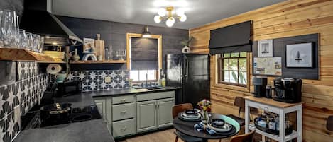 Una cocina compacta con un refrigerador negro, una mesa de comedor con sillas y una cafetera.