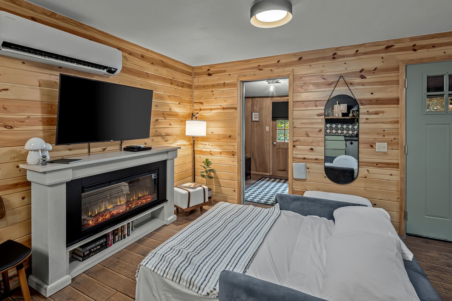 A modern log cabin bedroom with a fireplace, a flat-screen TV, a bed, and a mirror.