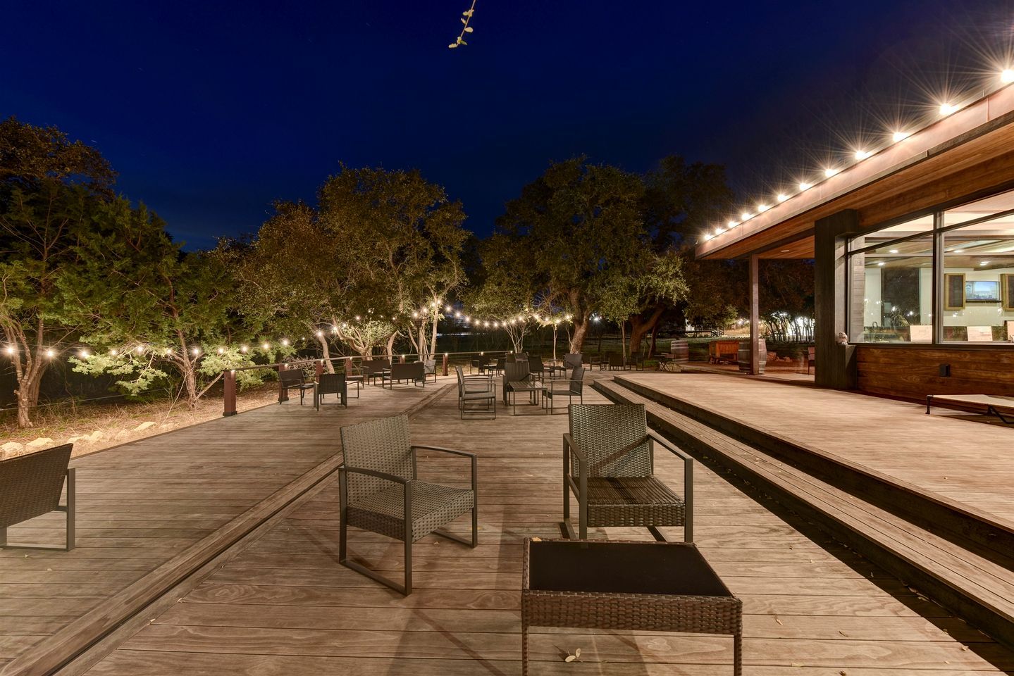 An outdoor patio area with seating, string lights, and a building with large windows.