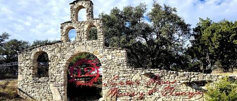 A stone structure with arches and a tower, surrounded by trees.