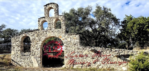 A stone structure with arches and a tower, surrounded by trees.