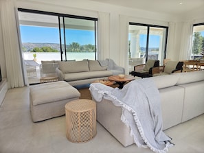 Ein modernes Wohnzimmer mit einer großen Couch, einem Couchtisch und Blick auf eine Küstenlandschaft durch große Fenster.