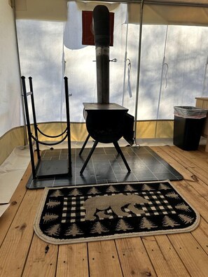 Un poêle à bois avec une cheminée, un tapis et une poubelle dans une pièce dont le sol est recouvert de carreaux.