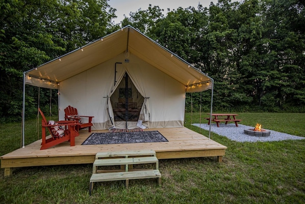 A tent with a bed, a red chair, a picnic table, and a fire pit.