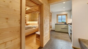 Ein Holzinterieur mit einem Bett, einem kleinen Tisch und einer Küchenzeile mit Schränken und einem Fenster.