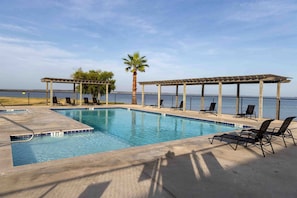 Ein Pool mit Liegestühlen, einer Palme und Blick auf das Wasser.