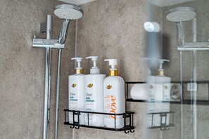 Un baño con ducha, espejo y repisa que contiene productos Dove para el cuidado de la piel.