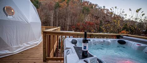 A hot tub on a wooden deck with a view of a tent and autumn trees.