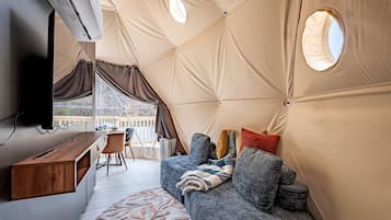A tent with a wooden desk, a couch, and a TV mounted on the wall.