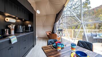 A modern kitchen with a dining area, a tented outdoor space, and a view of trees.