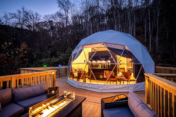 A dome-shaped tent with a wooden deck, outdoor seating, and a fire feature.