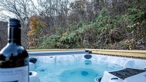 Un jacuzzi con una terraza de madera y una botella de vino en primer plano.