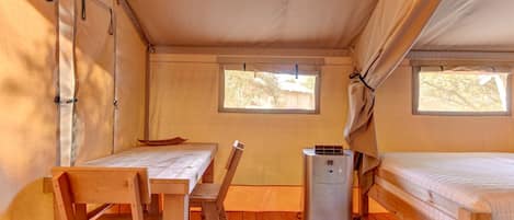Una carpa con una mesa de madera, una silla, un equipo de aire acondicionado pequeño y una cama.