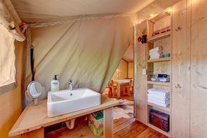 Ein Zeltraum mit Waschbecken, Spiegel und Stauraumschrank.