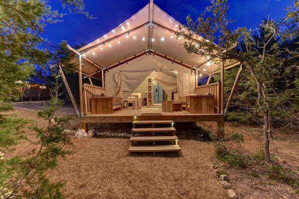 Alojamiento tipo tienda con terraza de madera, una escalera que lleva a la entrada y luces colgantes.