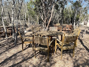 An outdoor dining area with wooden tables and chairs, surrounded by trees. - Amazing Tented Cabin with Awesome Sights in Johnson City, Texas (Johnson City)