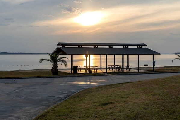 A covered picnic area with benches and a trash can, overlooking a body of water.