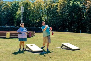 Dos personas jugando un juego en un campo cubierto de césped con dos mesas de juego de shuffleboard.