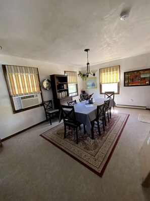 A dining area with a table, chairs, a chandelier, and a rug. - Cottage Rental on Chappaquiddick Island with Transferable Ferry Ticket Availability Massachusetts (Edgartown)