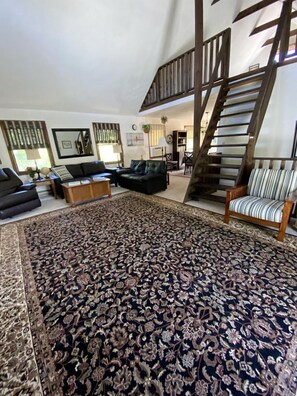 Amplia sala de estar con un tapete estampado, una escalera y muebles modernos.