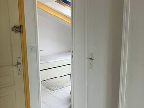 Una puerta blanca que da a una habitación con cama, una ventana pequeña y un techo con viga de madera.