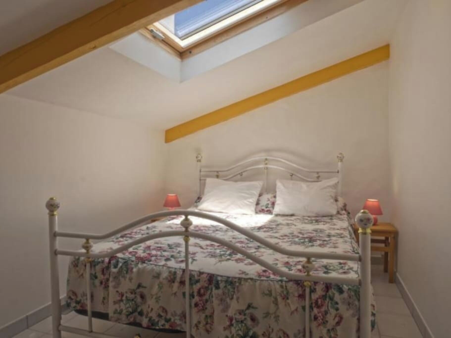 A bedroom with a skylight, a bed with a floral bedspread, two bedside lamps, and a wooden headboard.