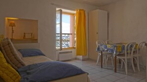Une chambre à coucher avec un lit, une fenêtre avec des rideaux, une table avec des chaises et une armoire.