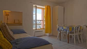 A bedroom with a bed, a window with curtains, a table with chairs, and a wardrobe.
