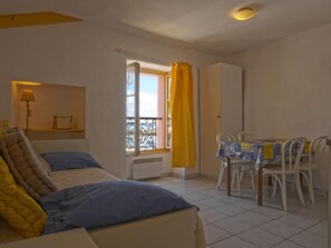 Un dormitorio con cama, ventana con cortinas, mesa con sillas y armario.