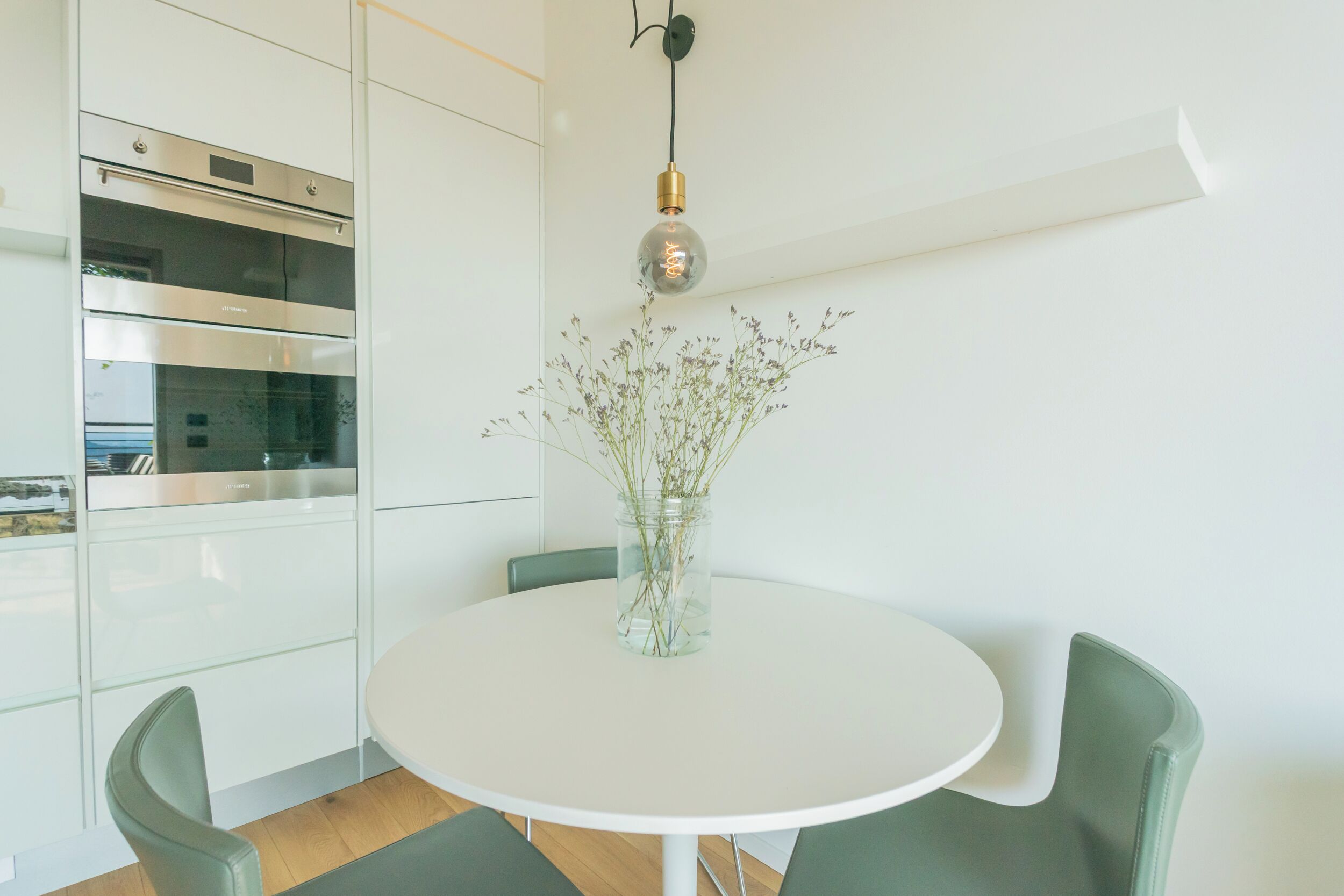 A modern kitchen with white cabinets, stainless steel appliances, and a round table with chairs.