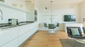 A modern kitchen with white cabinets, a dining area with a round table and chairs, a TV mounted on the wall, and a wooden floor. - Skyline Lake Apartment (Como)