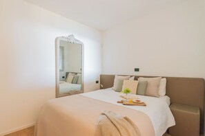 A bedroom with a large mirror, a bed with a white bedspread, pillows, a bedside table with a vase of flowers, and a tray with a glass of orange juice. - Skyline Lake Apartment (Como)