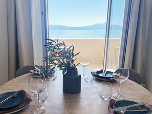 A dining table with plates, cutlery, and wine glasses set for two, with a view of the sea and mountains through large windows. - Relaxation with a view and close to the beach, Zaostrog VistaBlu (Zaostrog)