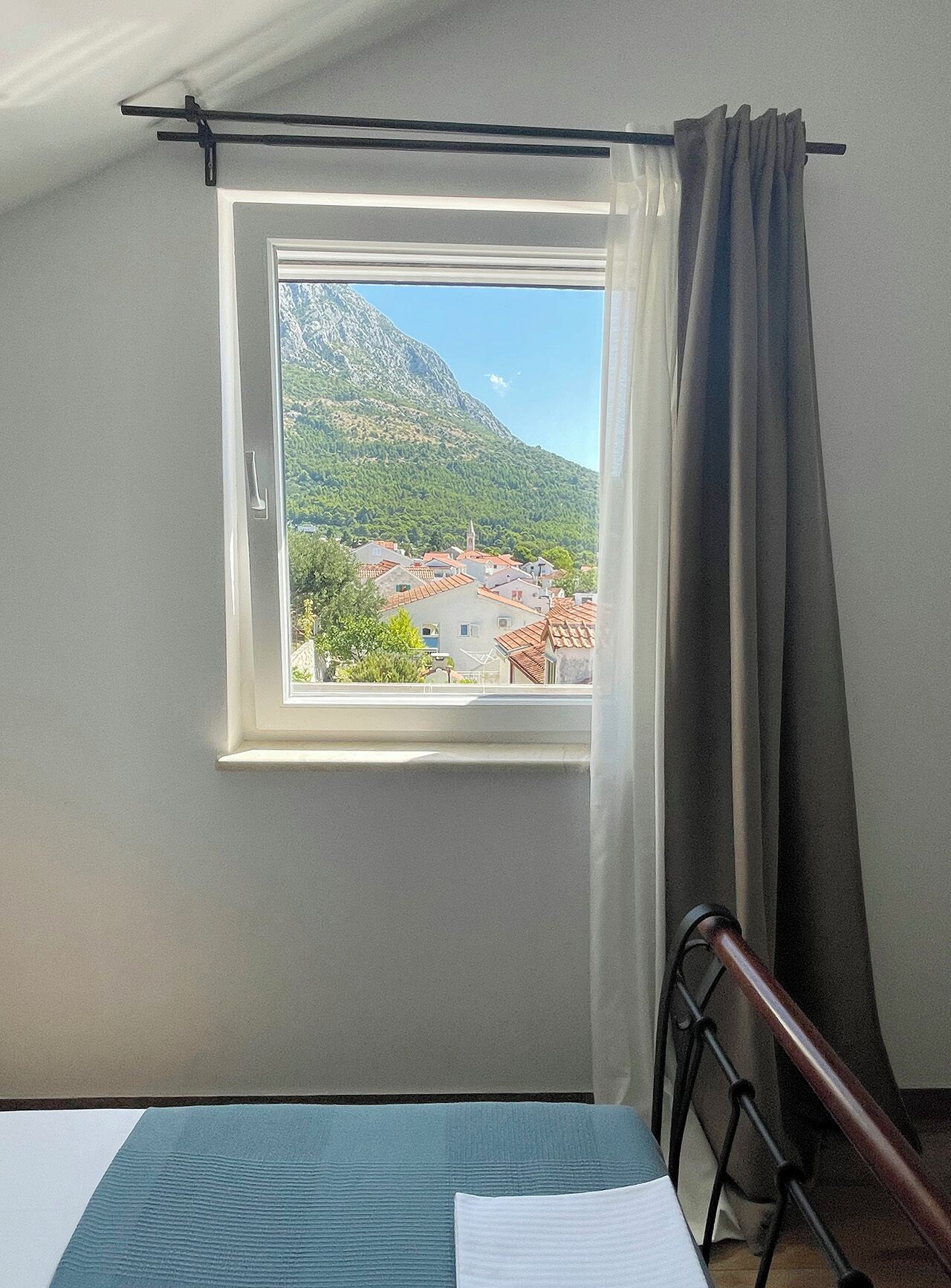 Habitació amb finestra que dona a un paisatge de muntanya, un llit i una cadira.