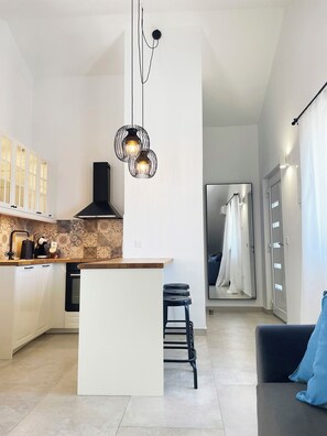 A modern kitchen with a central island, a dining area with a black chair, and a view into a bedroom with a white door. - Relaxation with a view and close to the beach, Zaostrog VistaBlu (Zaostrog)