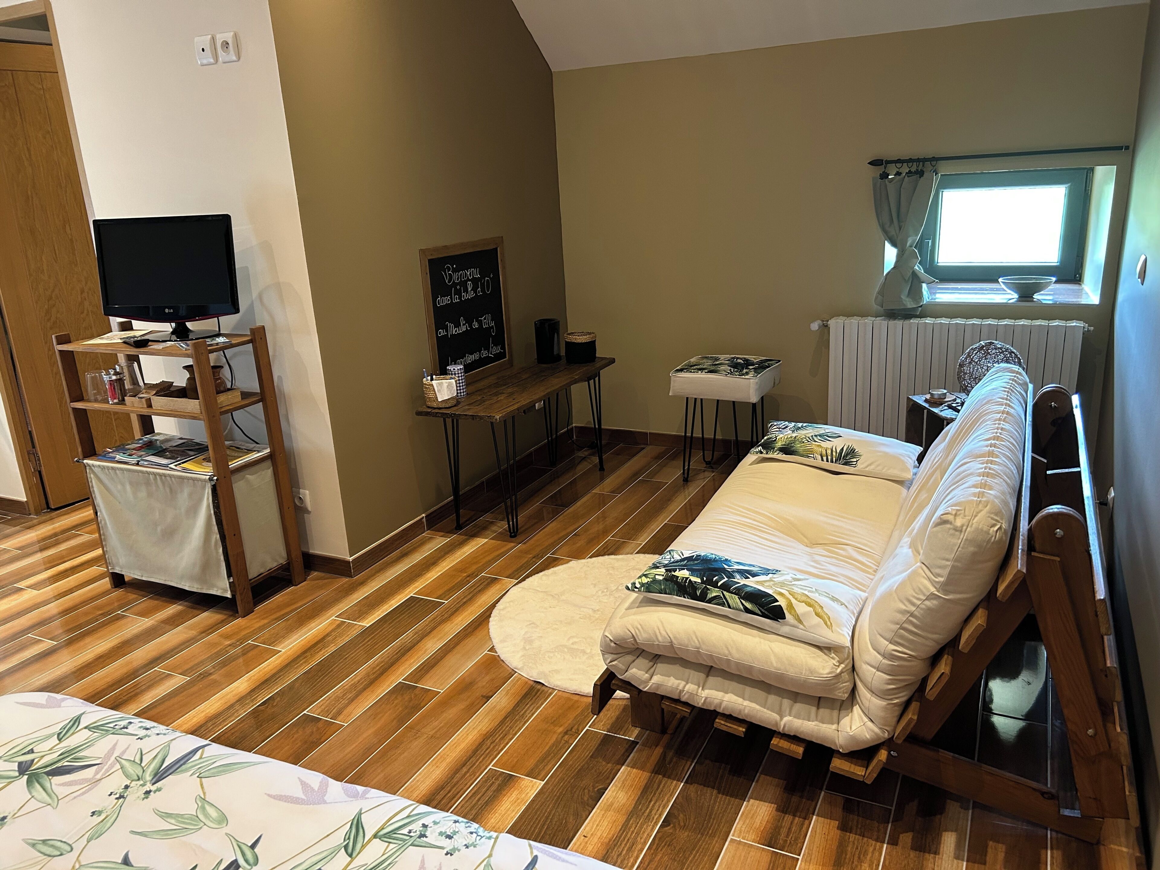 Quarto com sofá, televisão em uma estante, uma mesinha e janela com cortinas.