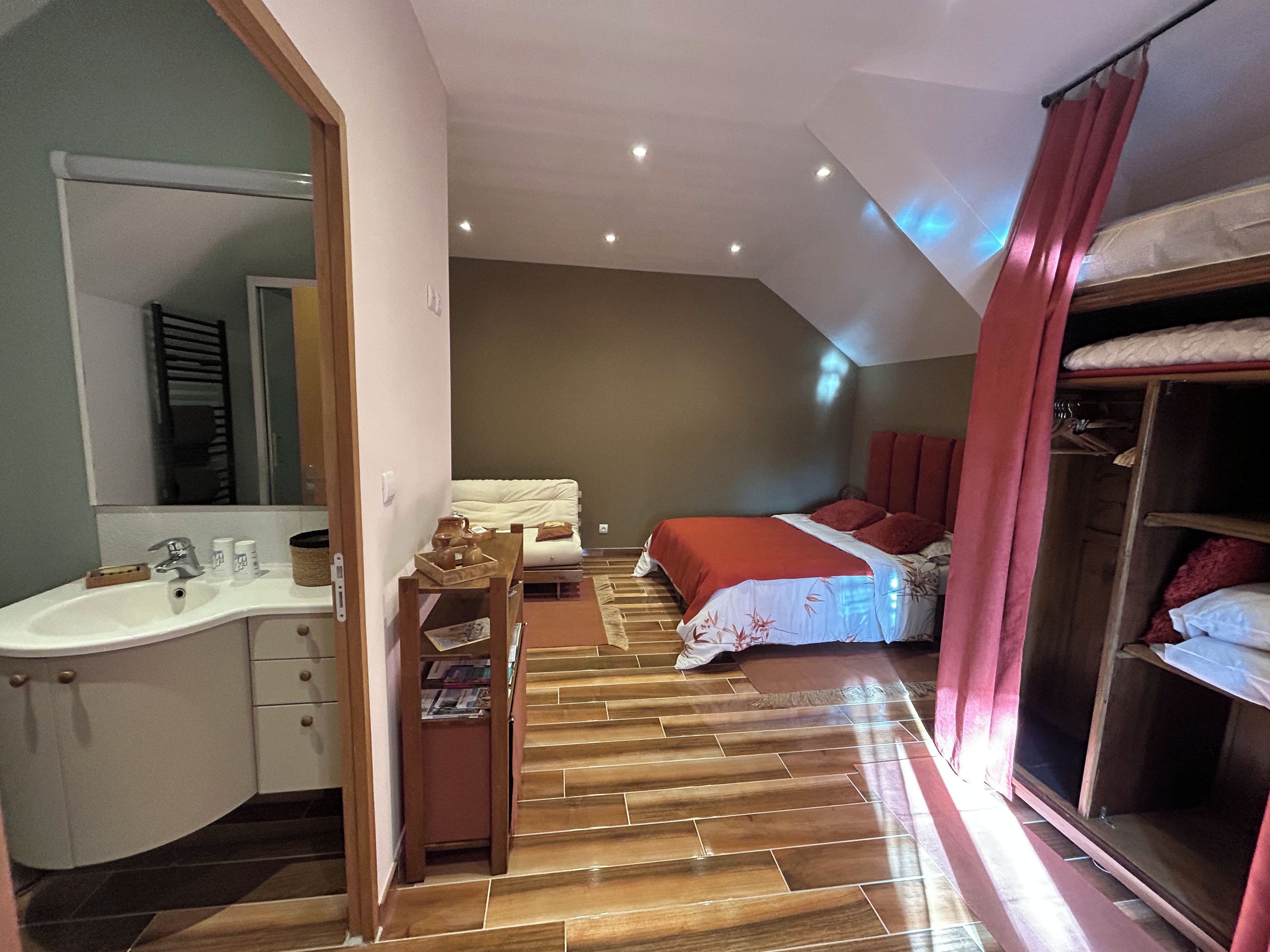 A bedroom with a wooden floor, a bed with red bedding, a bedside table, and a wardrobe.